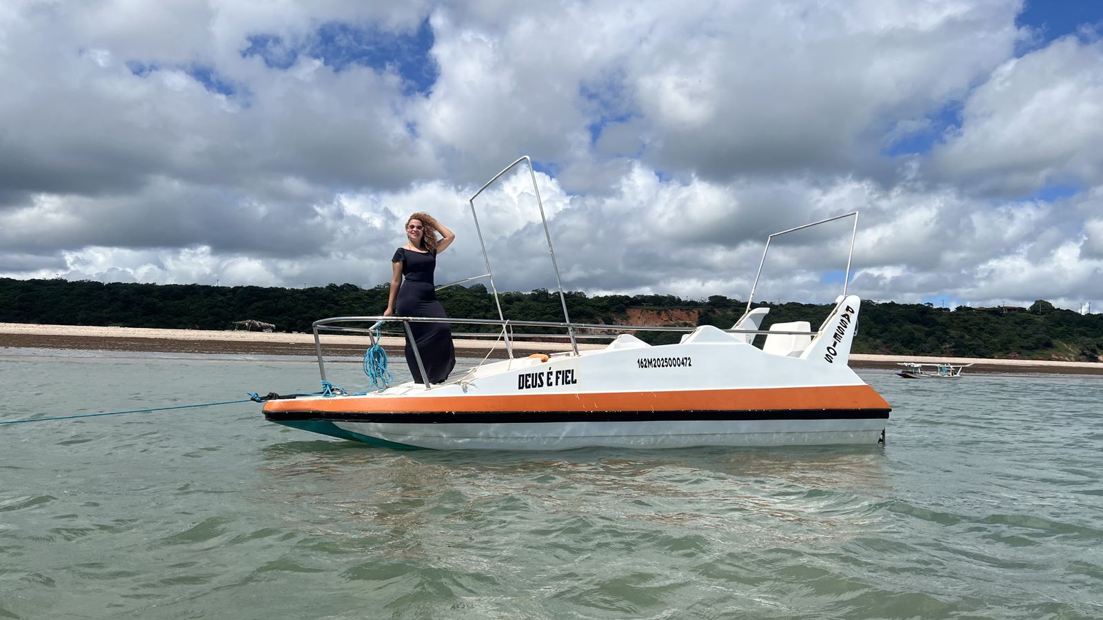 Lancha Deus é Fiel ancorada em frente à praia com falésias ao fundo